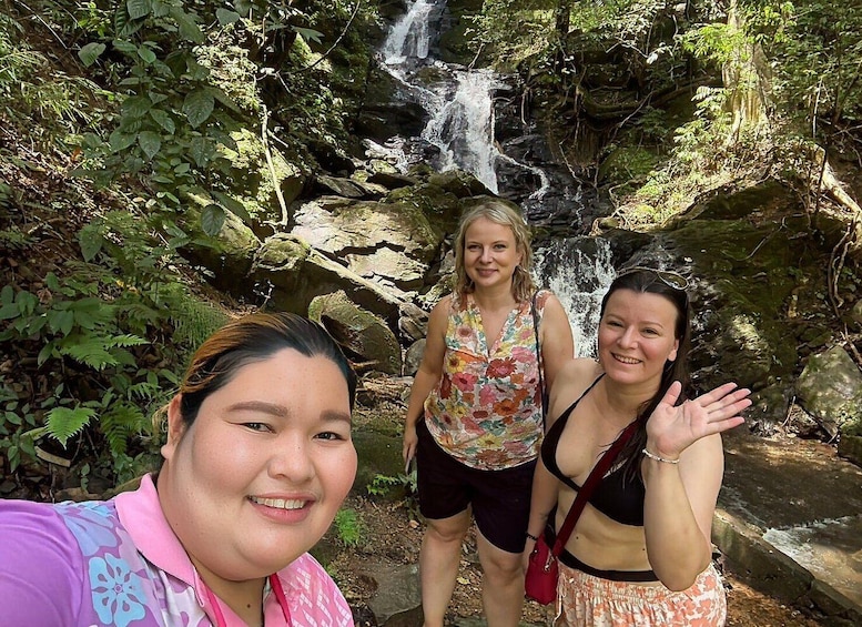 Three people standing in front of a waterfall surrounded by greenery. 5