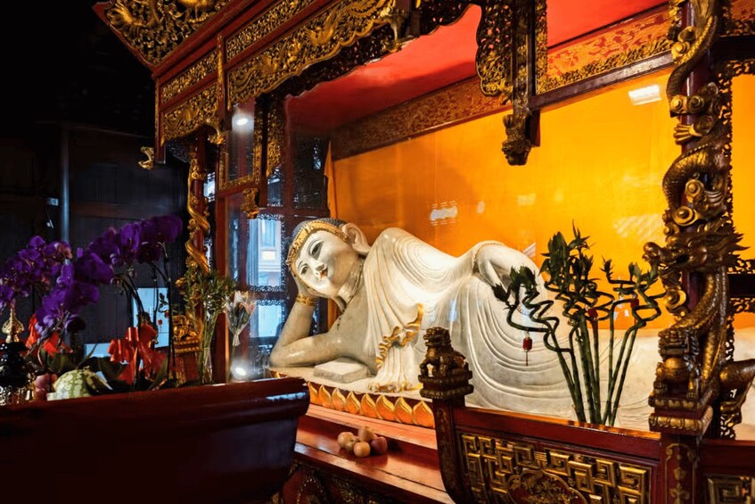 A statue of a reclining figure in a temple setting with ornate golden decorations and purple flowers. 2