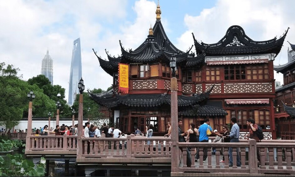 A traditional Chinese pavilion with ornate roofs and a crowd of people on a bridge. 1