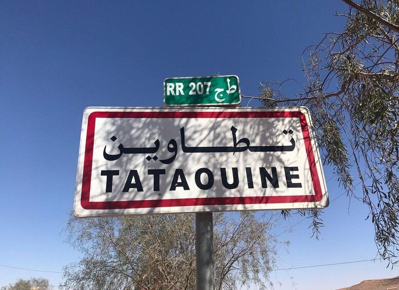 Ein Straßenschild mit 'TATAOUINE' und 'RR 207', beides in Arabisch und Englisch. 1