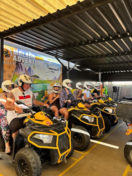 A group of people on ATVs in a covered parking area with a mural advertising a tour. 2