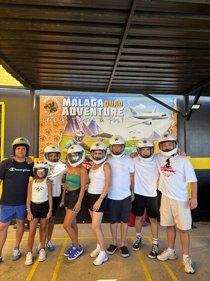 A group of people in helmets and casual clothing posing in front of a 'Malaga Quad Adventure' sign. 5
