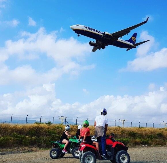 A RyanAir plane flying overhead, a person on a green ATV, and another on a red ATV. 4