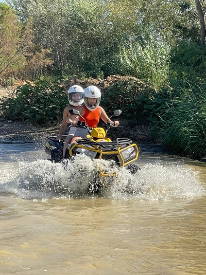 Two people on a yellow ATV crossing a shallow river. 3