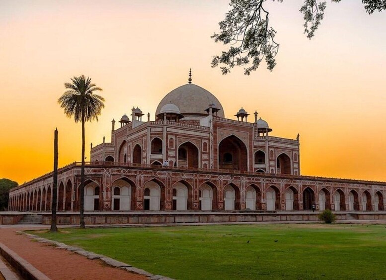 A large, historic building with a central dome and multiple smaller domes, surrounded by a well-maintained lawn and palm trees. 1