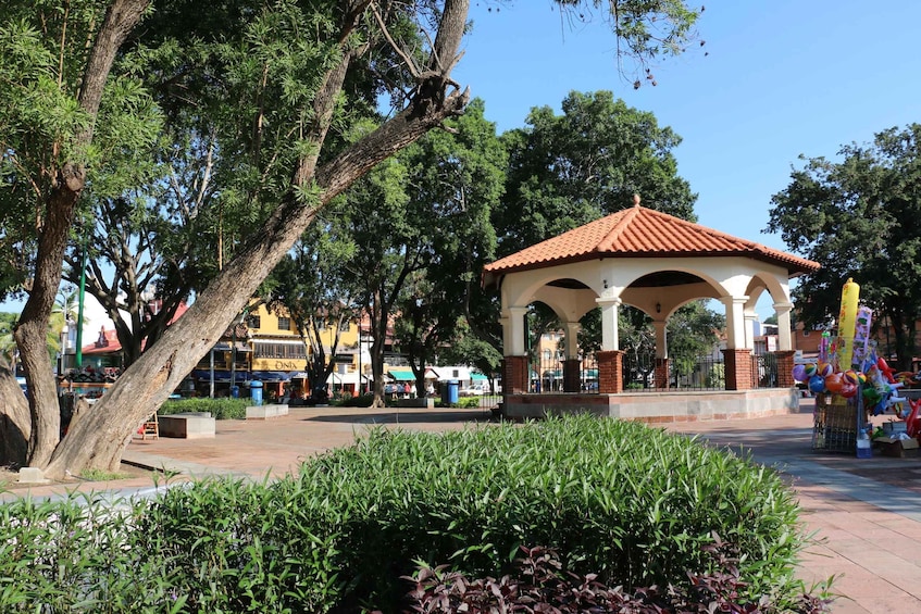 A gazebo in a park with trees and a clear sky. 2
