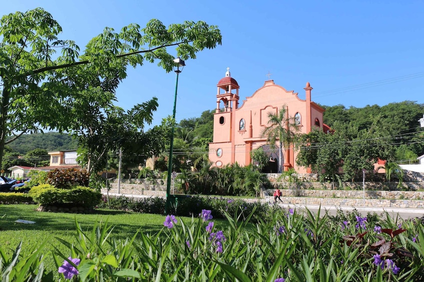 A pink church with a bell tower, surrounded by greenery and a clear blue sky. 4