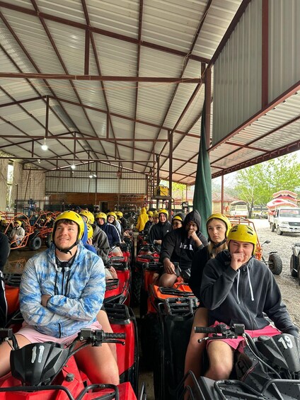 People in helmets on ATVs inside a covered area with a metal roof. 4