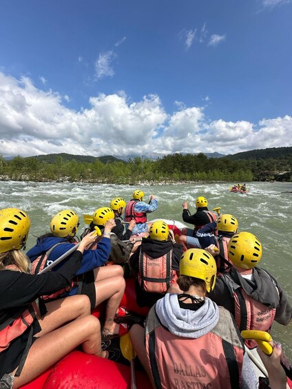 A group of people rafting on a river, wearing helmets and life jackets. 5