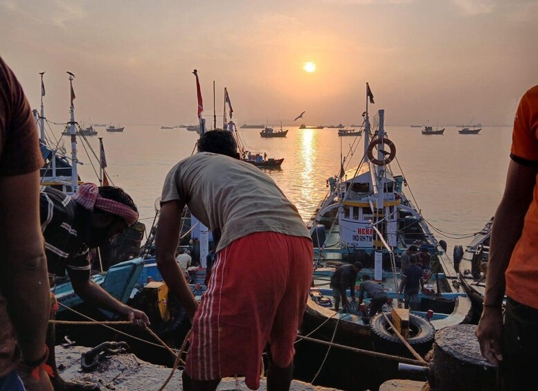 A sunset at a harbor with boats docked and people working. 1