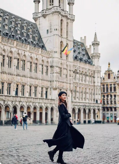 A woman in a black coat walking in front of a historic building with multiple towers and flags. 1