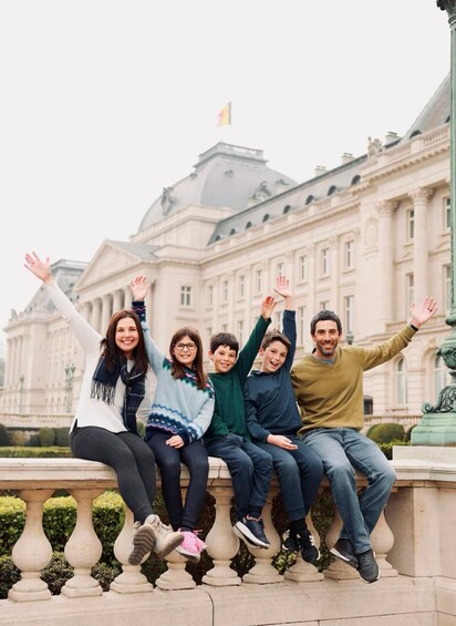 A group of people sitting on a balustrade with a large building in the background. 2