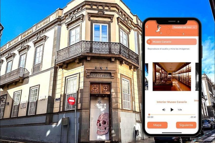 A smartphone displaying a museum tour app with a building labeled 'Museo Canario' in the background. 3