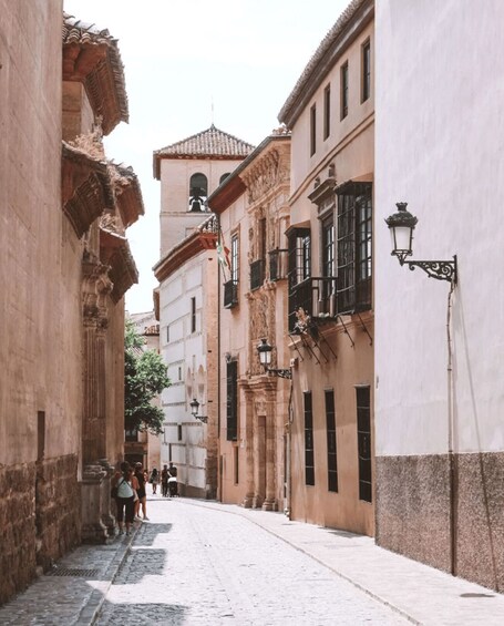 A narrow cobblestone street flanked by historic buildings with ornate facades and a clock tower in the distance. 2