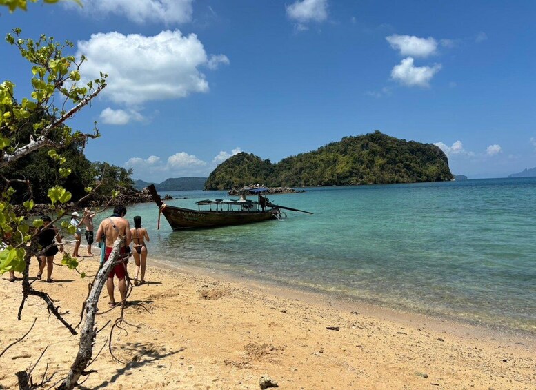 A beach with clear turquoise water, a boat near the shore, and a forested island in the background. 5