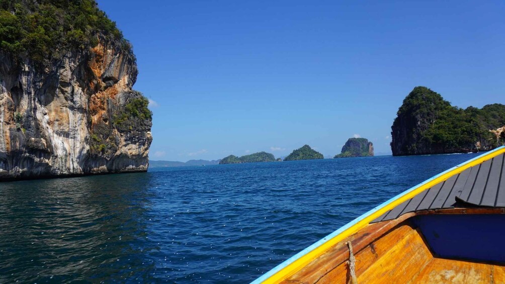 A boat on clear blue waters with rocky cliffs and small islands in the distance. 4