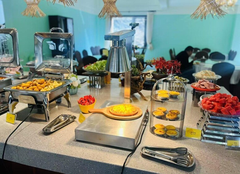 Monipuolinen buffet, jossa on tarjolla erilaisia ruokia, kuten hedelmiä, leivonnaisia ja kuuma grilli, jossa ruokia valmistetaan. 4