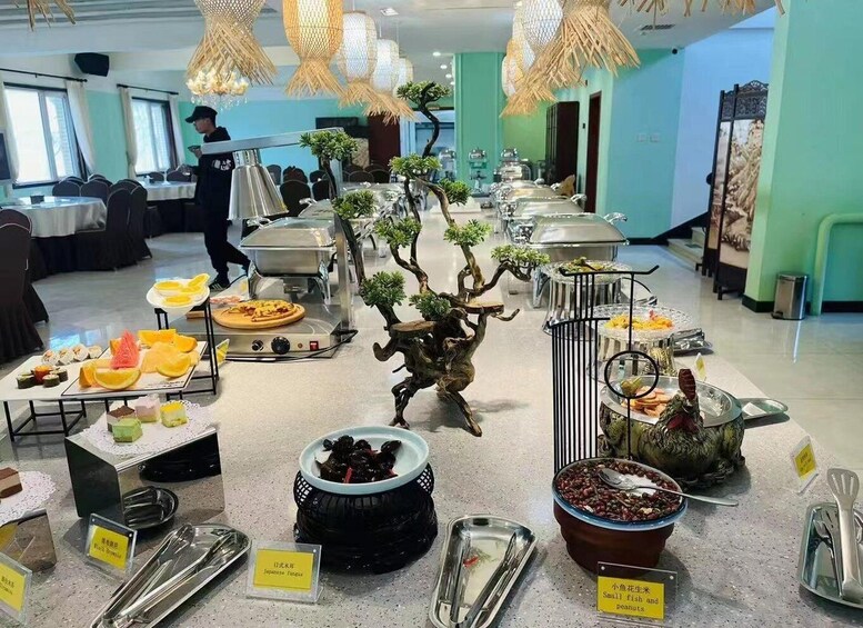 Tarjolla on monipuolinen buffet, pöydän keskellä on bonsaipuu, ja taustalla näkyy henkilö. 2