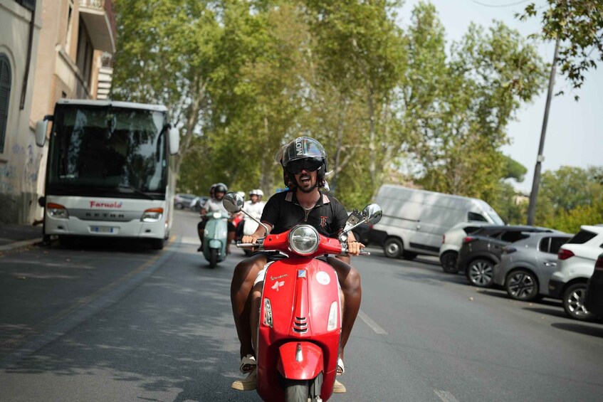A person riding a red scooter on a street with parked cars and a bus in the background. 4
