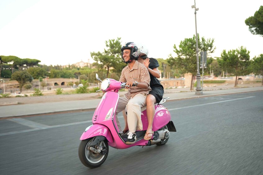 A pink scooter with two passengers, one adult and one child, on a road with trees and buildings in the background. 5