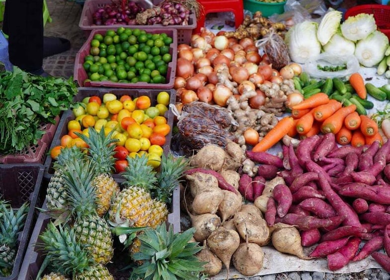 A variety of fresh produce including pineapples, sweet potatoes, carrots, and onions at a market stall. 3
