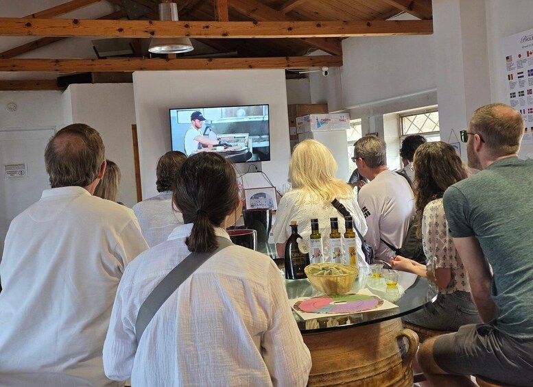 A group of people watching a chef cooking on a television screen in a room with wooden beams and a whiteboard. 4