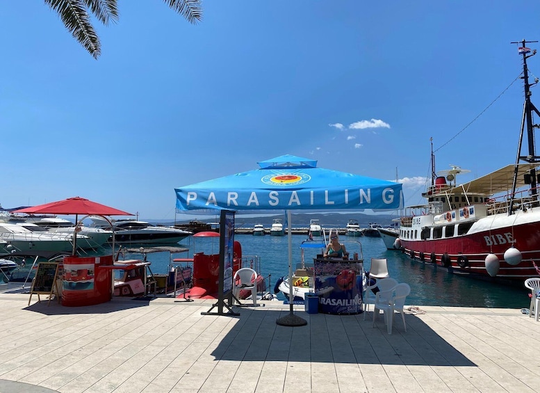 A parasailing setup with a blue canopy labeled 'PARASAILING' and a 'BIBE' boat in the background. 1