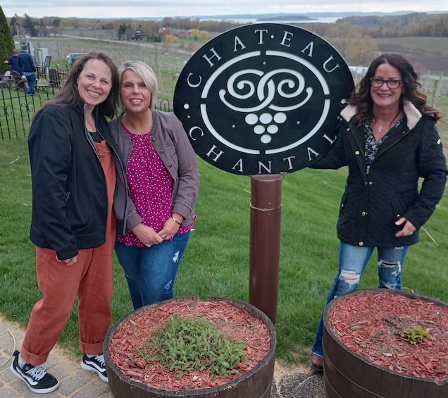 Three people standing in front of a sign that reads "CHATEAU CHANTAL." There are two large planters with plants in the foreground. 5