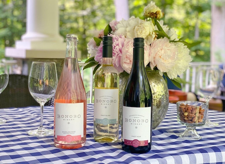 Three bottles of Bonobo Winery wine on a checkered tablecloth with a vase of flowers and a glass of nuts. 3