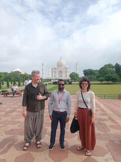 Three people standing in front of the Taj Mahal with a cloudy sky. 3