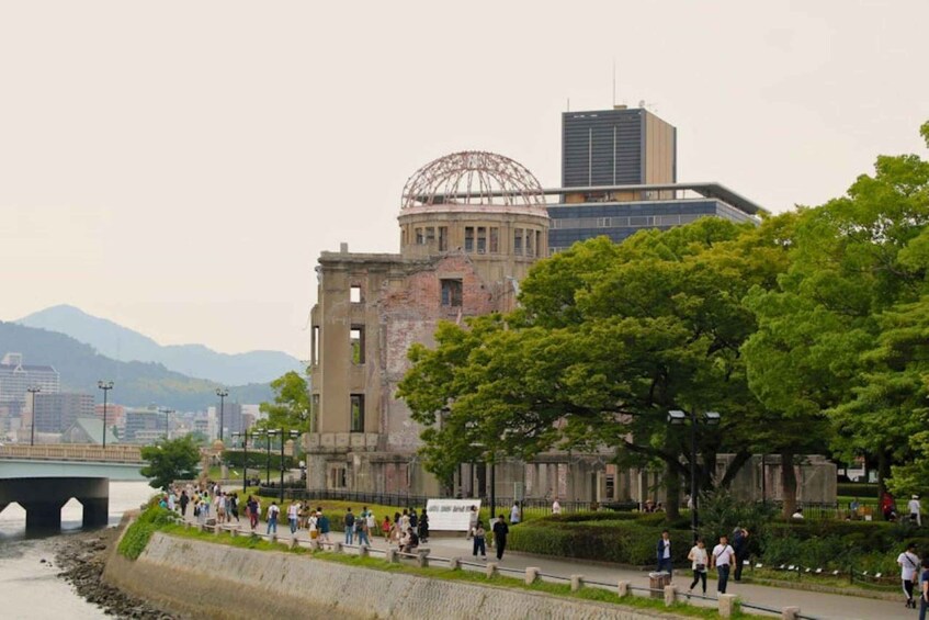 A riverside walkway with people walking, a historic building with a dome, and modern skyscrapers in the background. 4