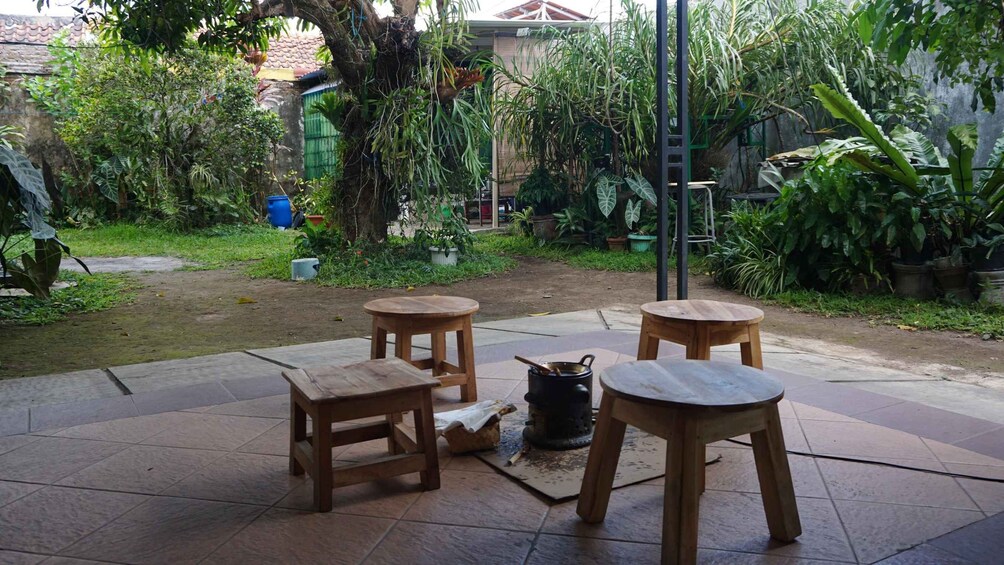 A patio with wooden stools and a table, surrounded by lush greenery and potted plants. 2
