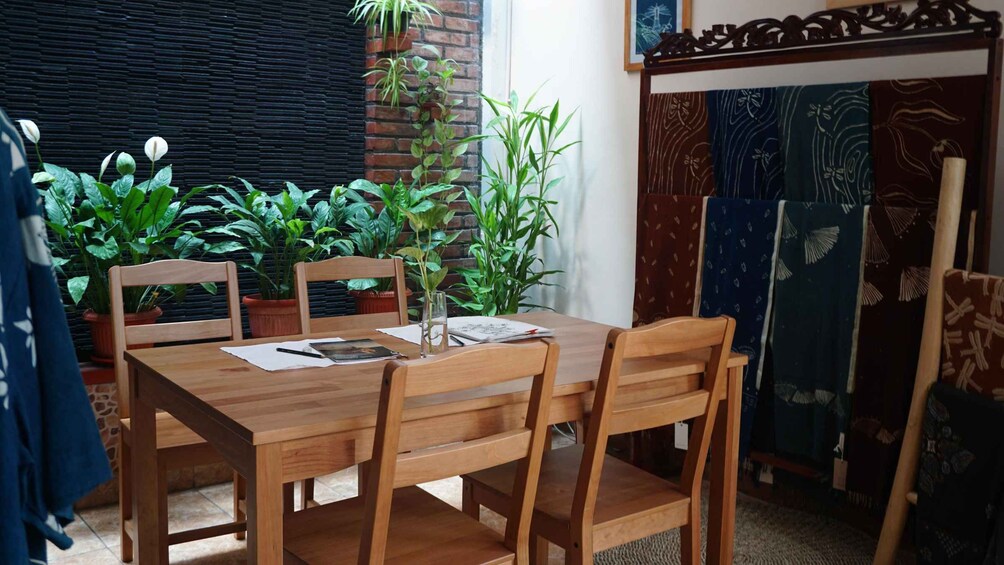 A wooden dining table with chairs, surrounded by potted plants, in a room with patterned curtains and a window. 3