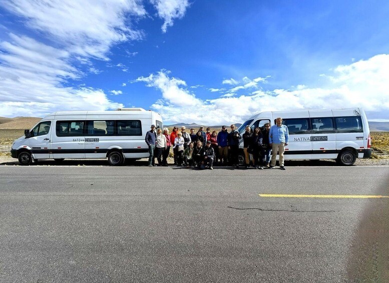 A group of people standing between two white vans with 'NATIVA EXPRESS' written on them, parked on a road with a clear sky and distant hills in the background. 4