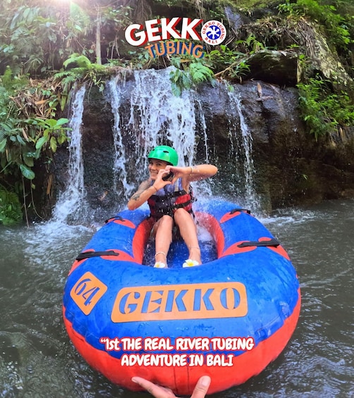A person in a blue and red raft with 'GEKKO' written on it, navigating a river with a waterfall in the background. 5