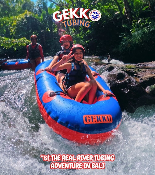 People rafting on a river with rapids, wearing helmets and life vests, and a blue and red raft with the GEKKO logo. 1