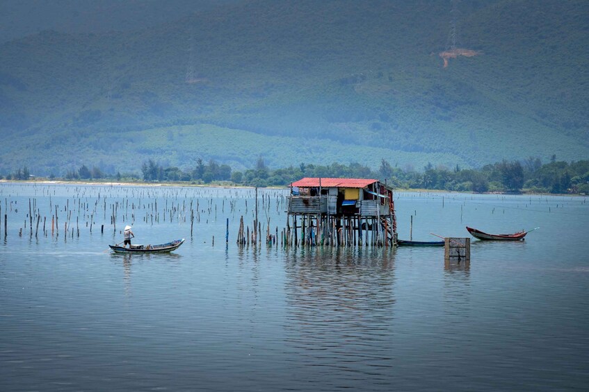A houseboat on a calm lake with a person rowing a small boat nearby and another boat anchored in the distance. 5