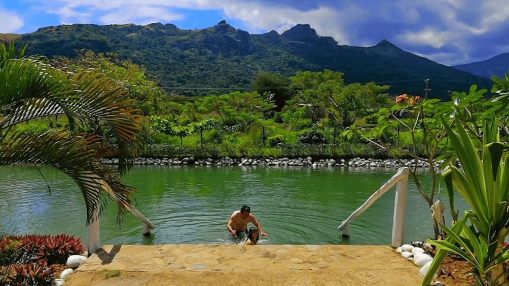 A man and a child playing in a natural pool surrounded by lush greenery and mountains. 2