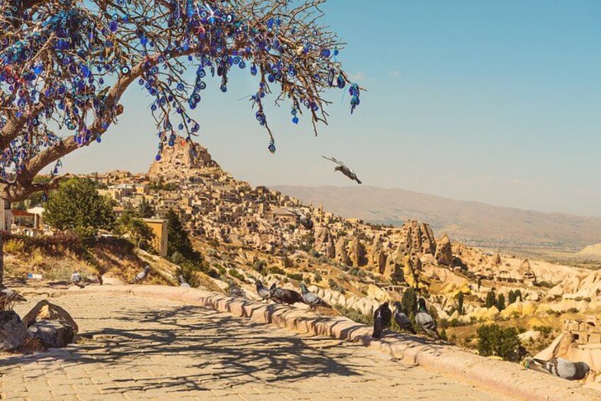 A rocky landscape with a tree bearing blue flowers, a bird in flight, and a distant view of a town. 3