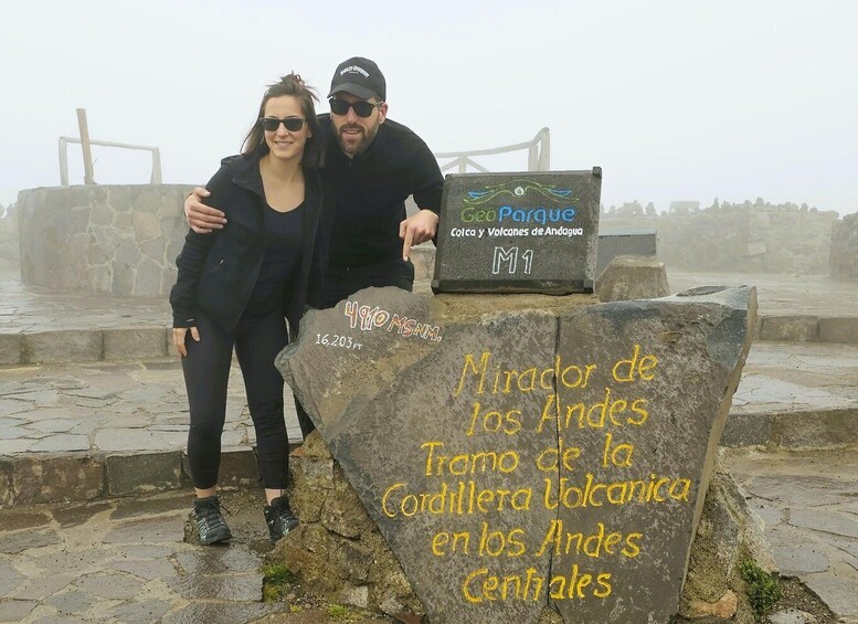 A couple standing on a stone platform with a sign indicating the location as 'Mirador de los Andes' and 'Fram de la Cordillera Volcanica en los Andes Centrales.' 5