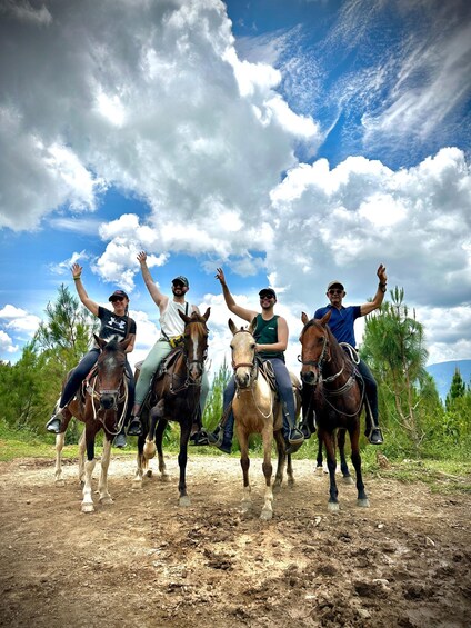 Four people riding horses on a dirt path with a cloudy sky above. 4
