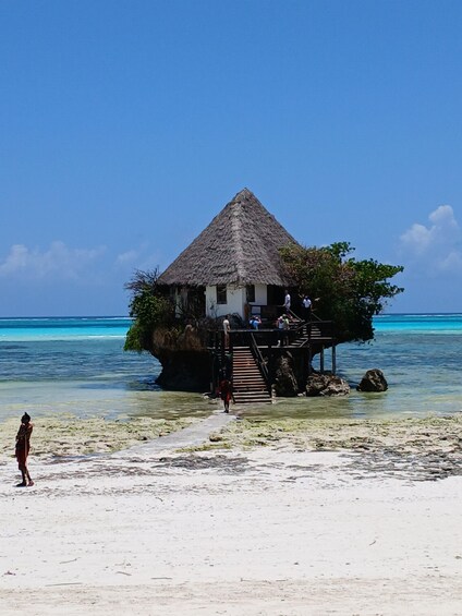 A thatched-roof structure on a beach with clear blue water. 1