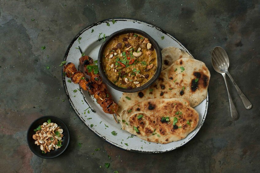 A plate with naan bread, a bowl of curry, and skewered meat. 1