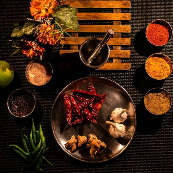 A variety of spices and herbs on a dark surface, including dried chilies, garlic, ginger, and turmeric. 3