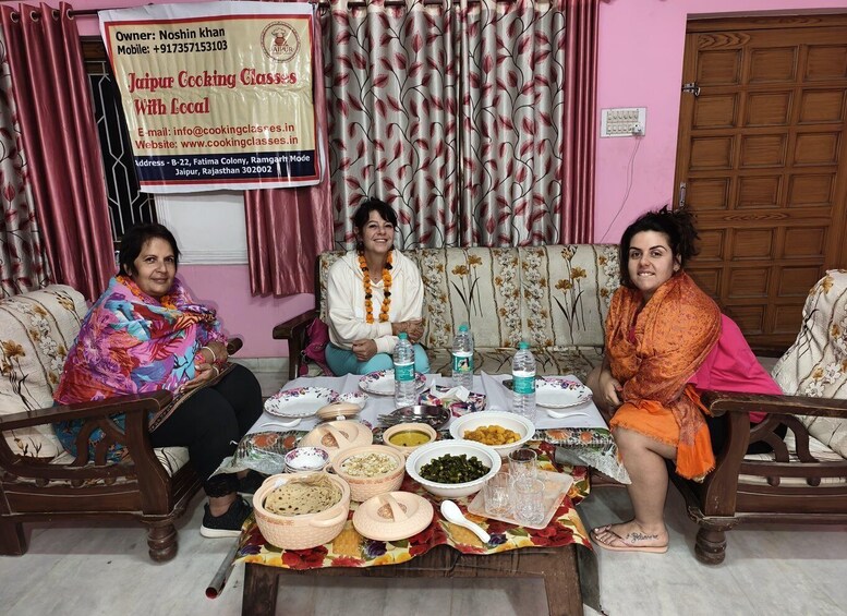 Three people sitting at a dining table with various dishes and a banner in the background. 4