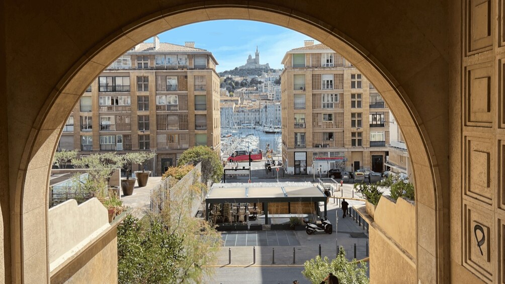 A view through an archway of a cityscape with buildings, a hilltop structure, and a body of water. 4