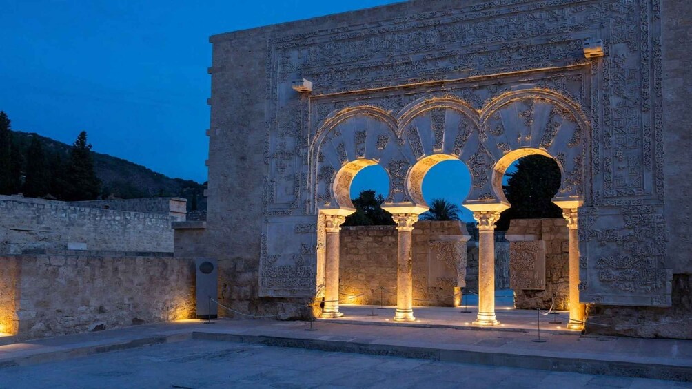 An ancient stone structure with ornate arches and columns, illuminated by artificial lighting. 1