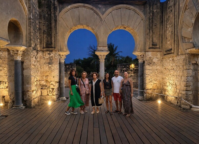 A group of people standing in front of an ancient stone archway with a wooden deck. 2