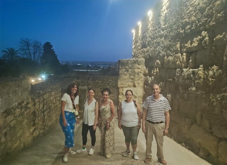 A group of people standing in front of ancient stone walls with lights illuminating the area. 3