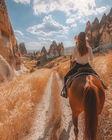 A person riding a horse on a dirt path through a rocky landscape with distinctive rock formations. 4